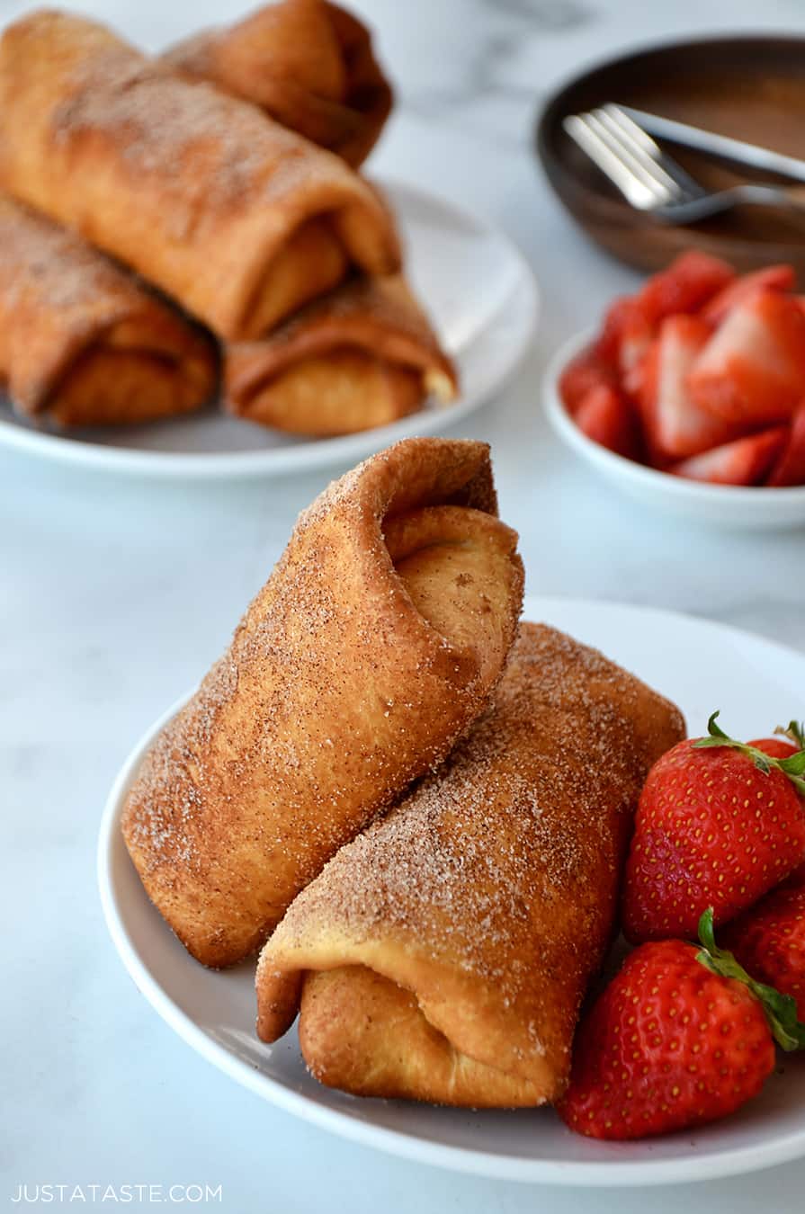 Two Strawberry Cheesecake Chimichangas on a white plate with fresh strawberries
