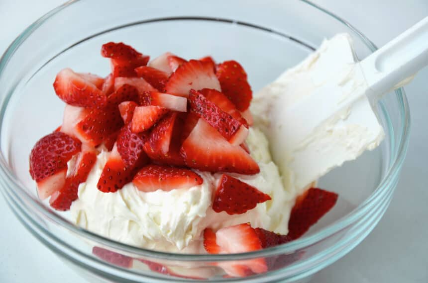 Spatula mixing cream cheese and fresh strawberries together in a clear bowl
