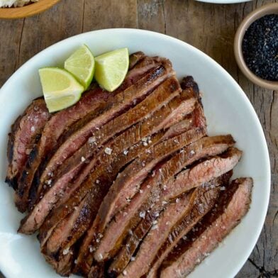 Sliced flank steak with the Ultimate Asian Flank Steak Marinade on white serving plate and lime wedges