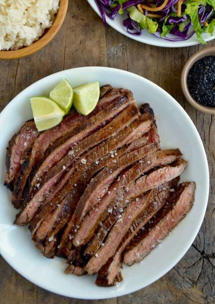 Sliced flank steak with the Ultimate Asian Flank Steak Marinade on white serving plate and lime wedges