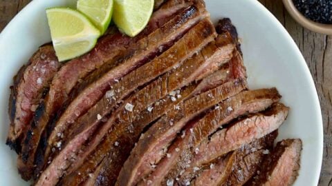 Sliced flank steak with the Ultimate Asian Flank Steak Marinade on white serving plate and lime wedges