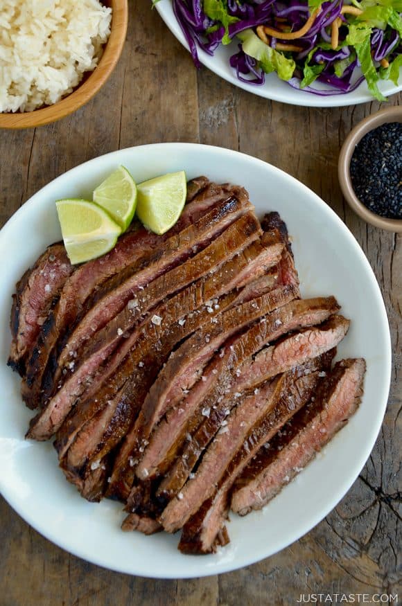 Sliced flank steak with the Ultimate Asian Flank Steak Marinade on white serving plate and lime wedges