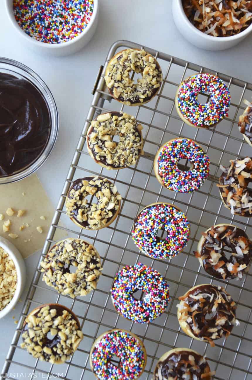 Baked Mini Buttermilk Doughnuts atop a wire cooling rack next to bowls containing Nutella Glaze and sprinkles