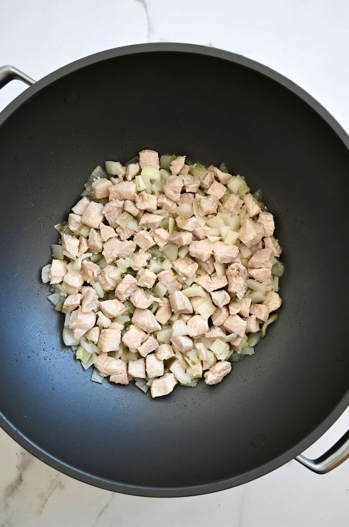 A wok containing cooked diced chicken breast with diced onions, and minced garlic and ginger.