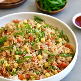 Pineapple chicken fried rice in a white bowl next to a small bowl filled with sliced scallions.