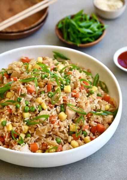 Pineapple chicken fried rice in a white bowl next to a small bowl filled with sliced scallions.