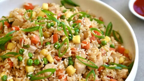 Pineapple chicken fried rice in a white bowl next to a small bowl filled with sliced scallions.