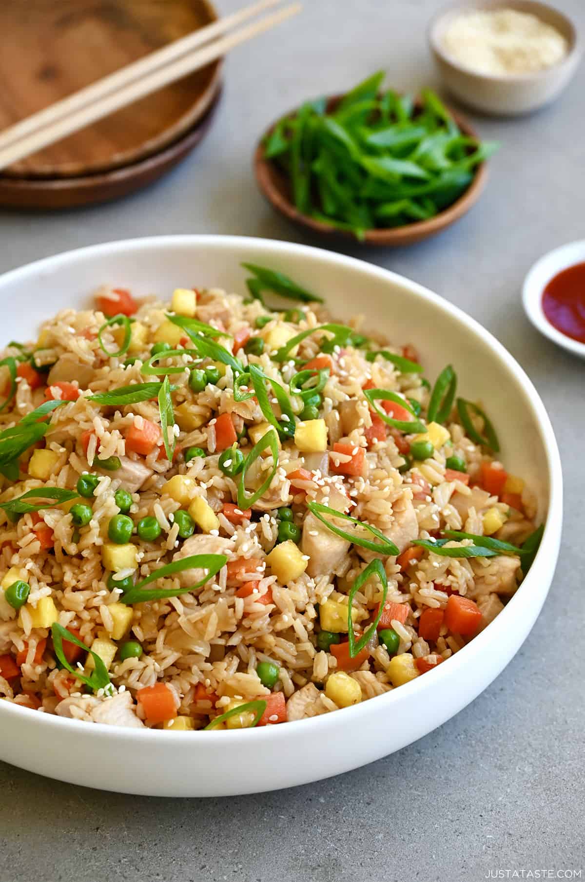 Pineapple chicken fried rice in a white bowl next to a small bowl filled with sliced scallions.