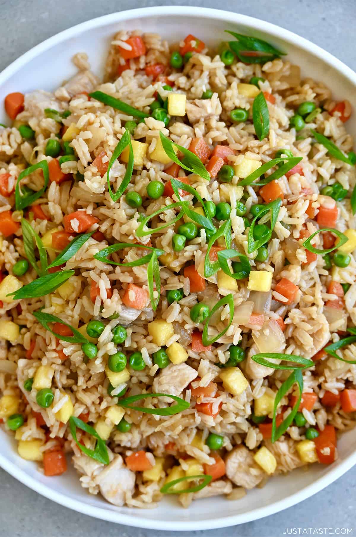 Pineapple chicken fried rice with peas and carrots in a white serving bowl.