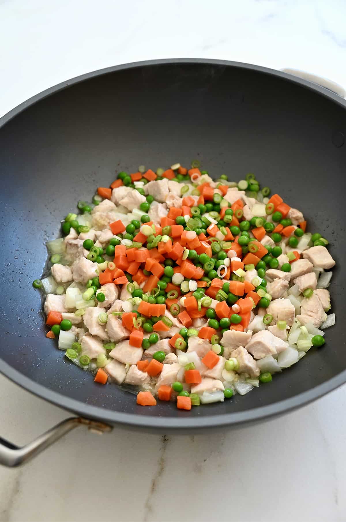 Peas and diced carrots with cooked chicken breast pieces in a wok.
