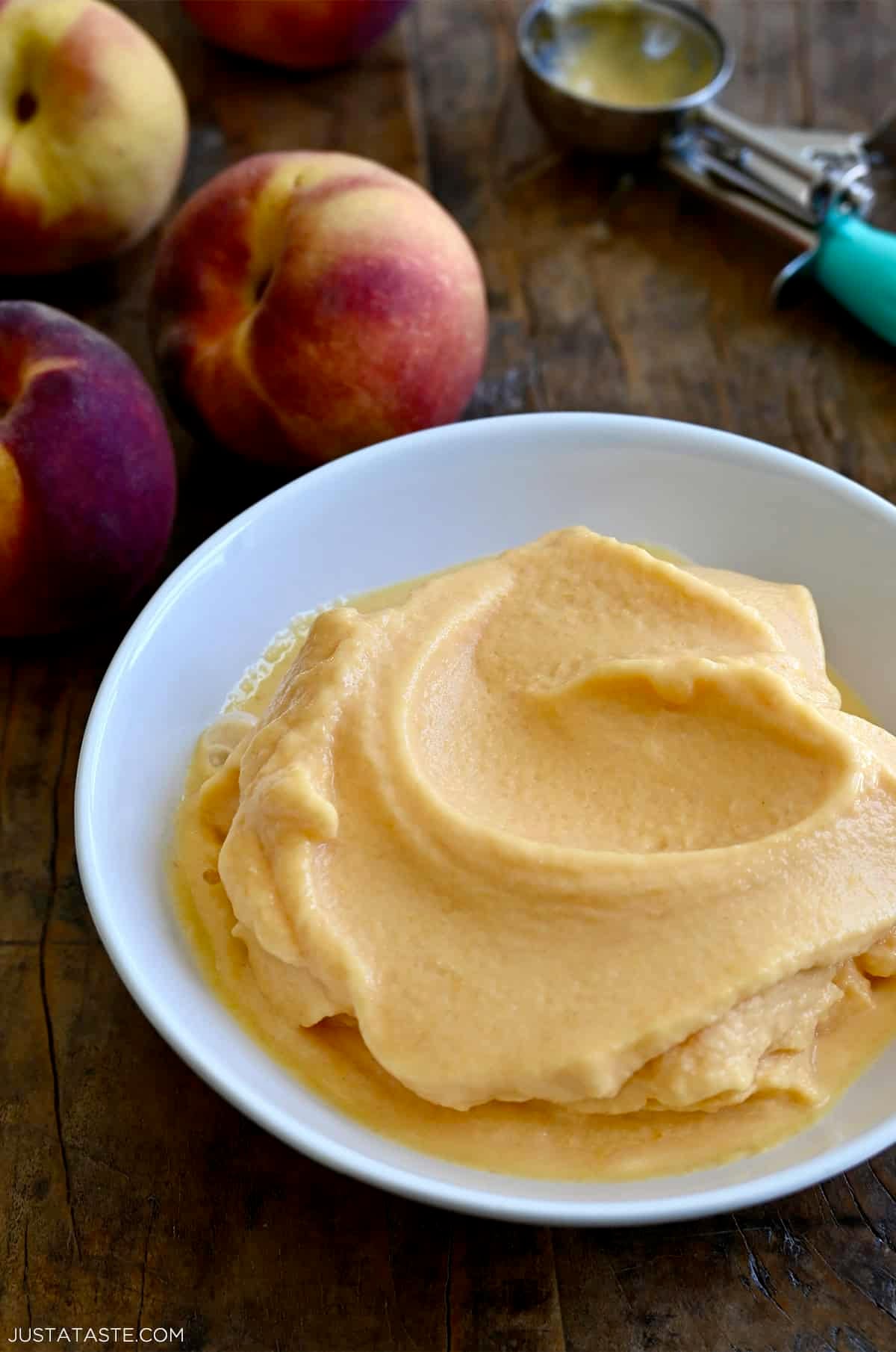 Homemade peach frozen yogurt in a bowl next to fresh peaches.