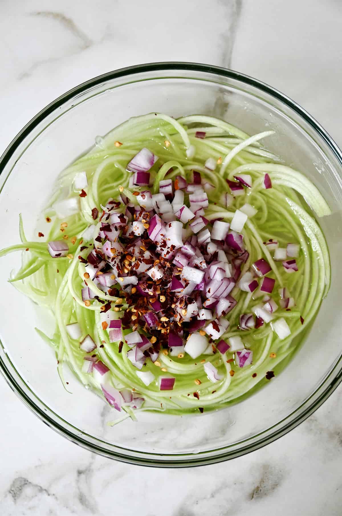 Crunchy Asian cucumber salad with a sweet and sour dressing, diced red onions, and chili flakes in a large glass bowl.