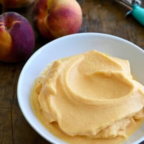 Cool and creamy 5-Minute Healthy Peach Frozen Yogurt in a white bowl next to fresh peaches