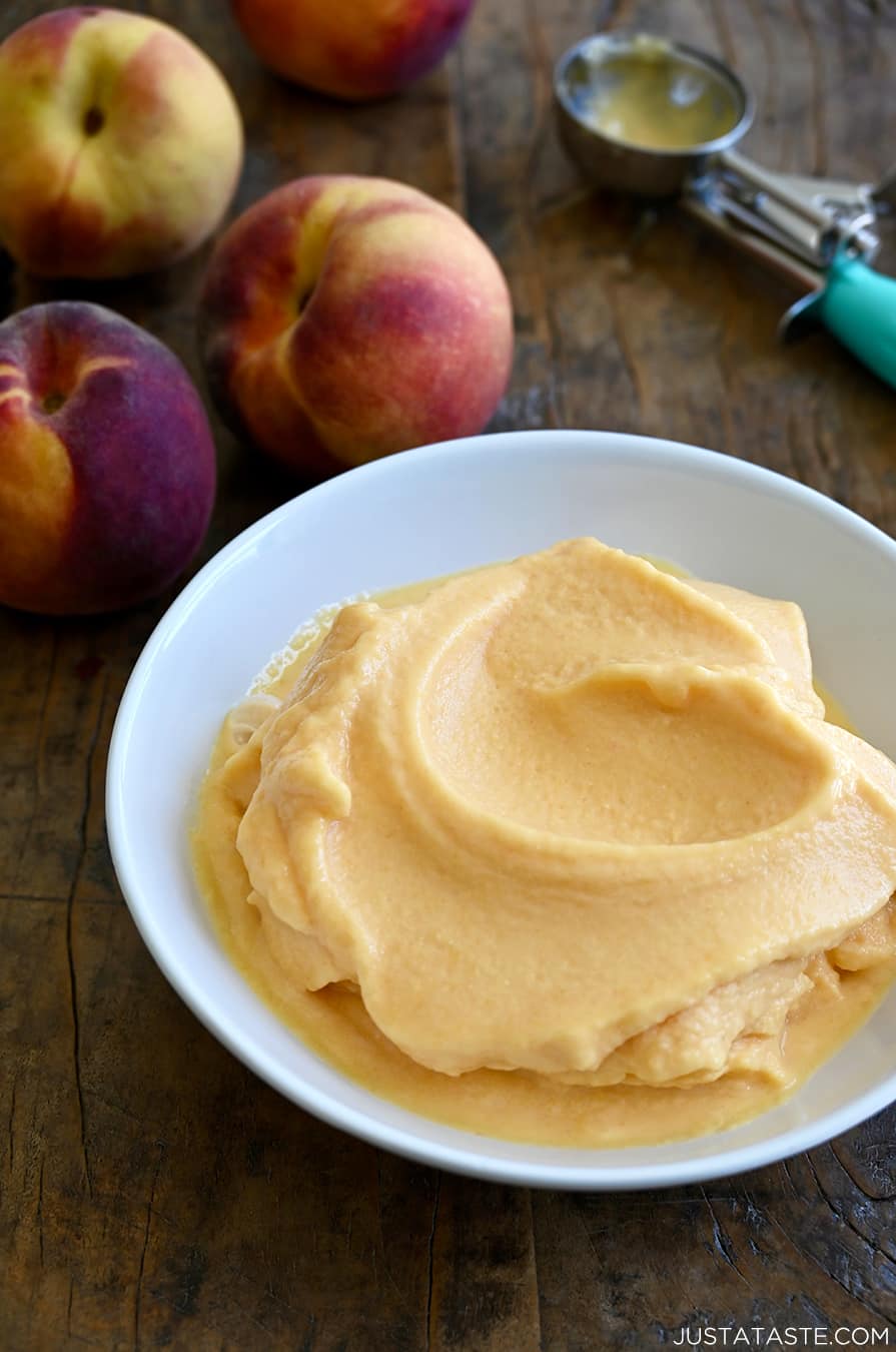 Cool and creamy 5-Minute Healthy Peach Frozen Yogurt in a white bowl next to fresh peaches