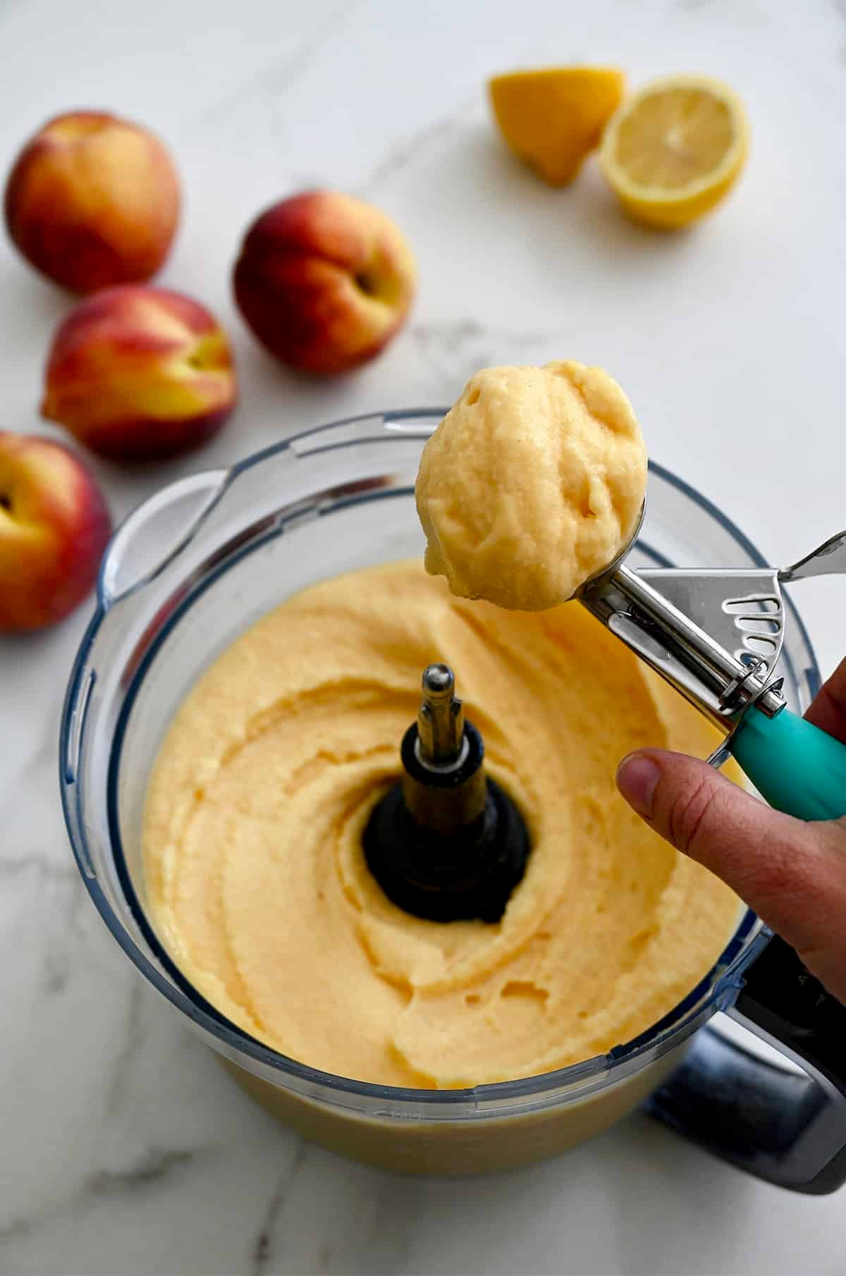 Soft-serve style peach frozen yogurt being scooped from a food processor.