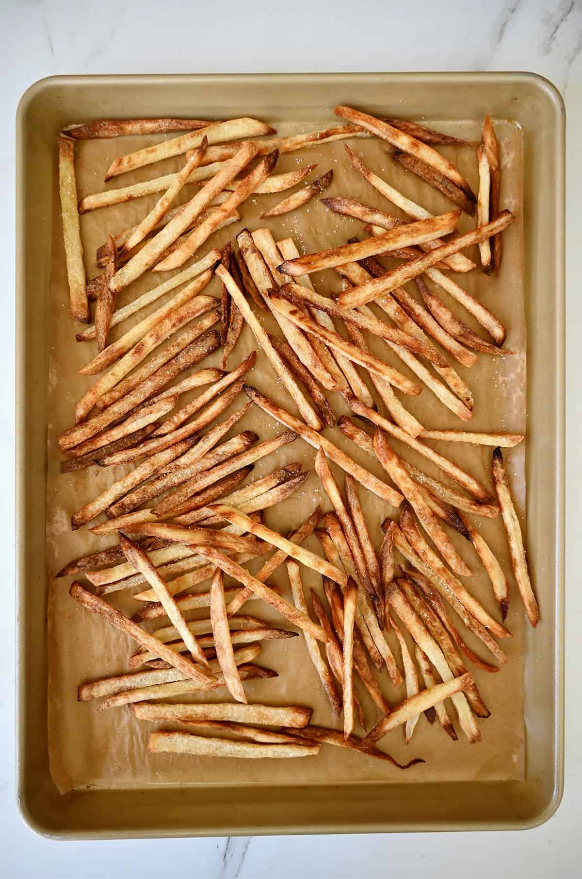 Crispy, golden brown baked fries on a parchment paper-lined baking sheet.