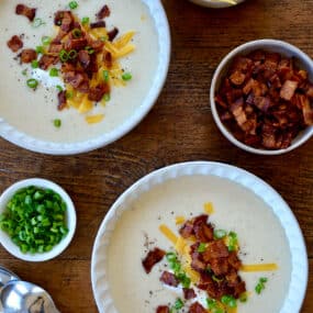 Top-down view of two white bowls containing Loaded Baked Potato Soup garnished with bacon, cheddar cheese and chopped scallions