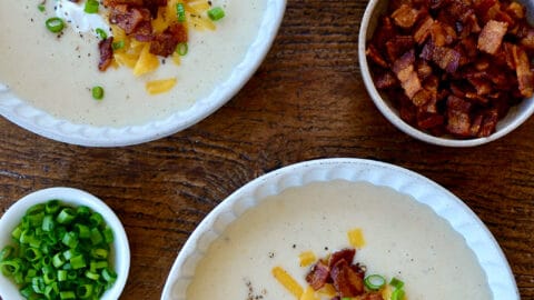 Top-down view of two white bowls containing Loaded Baked Potato Soup garnished with bacon, cheddar cheese and chopped scallions