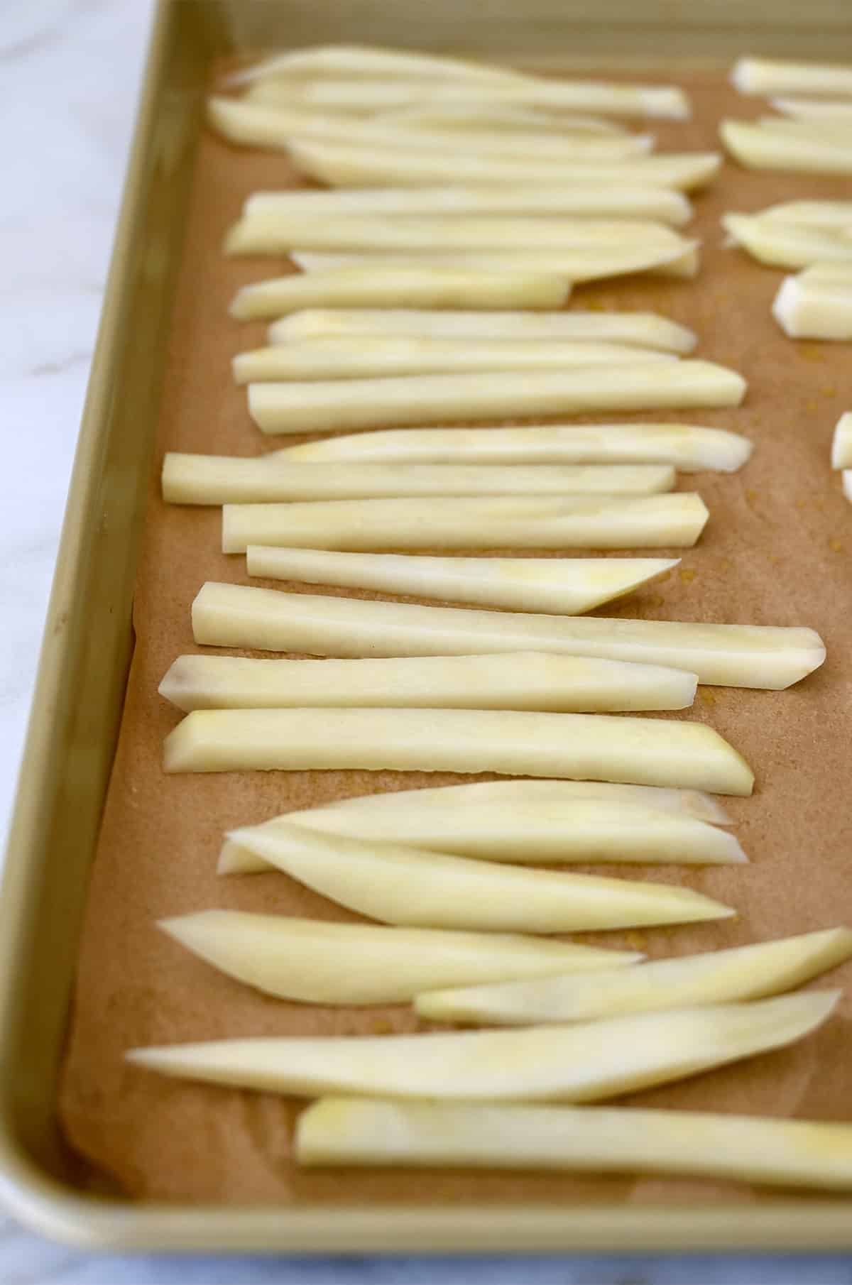 Unbooked fries on a parchment paper-lined baking sheet.