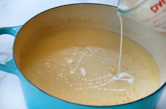 Heavy cream being poured into large stockpot filled with creamy soup