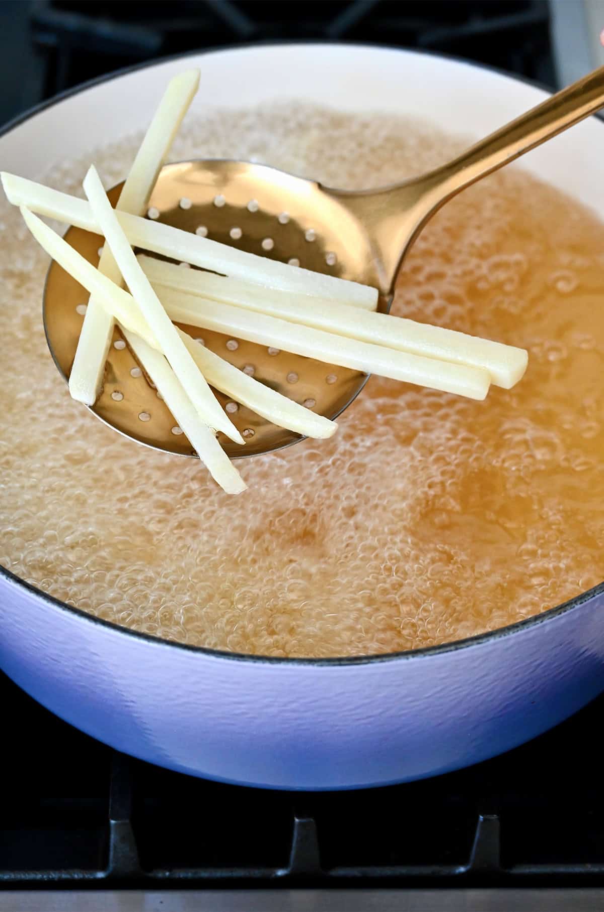 French fries on a slotted spoon over a Dutch oven with hot oil.