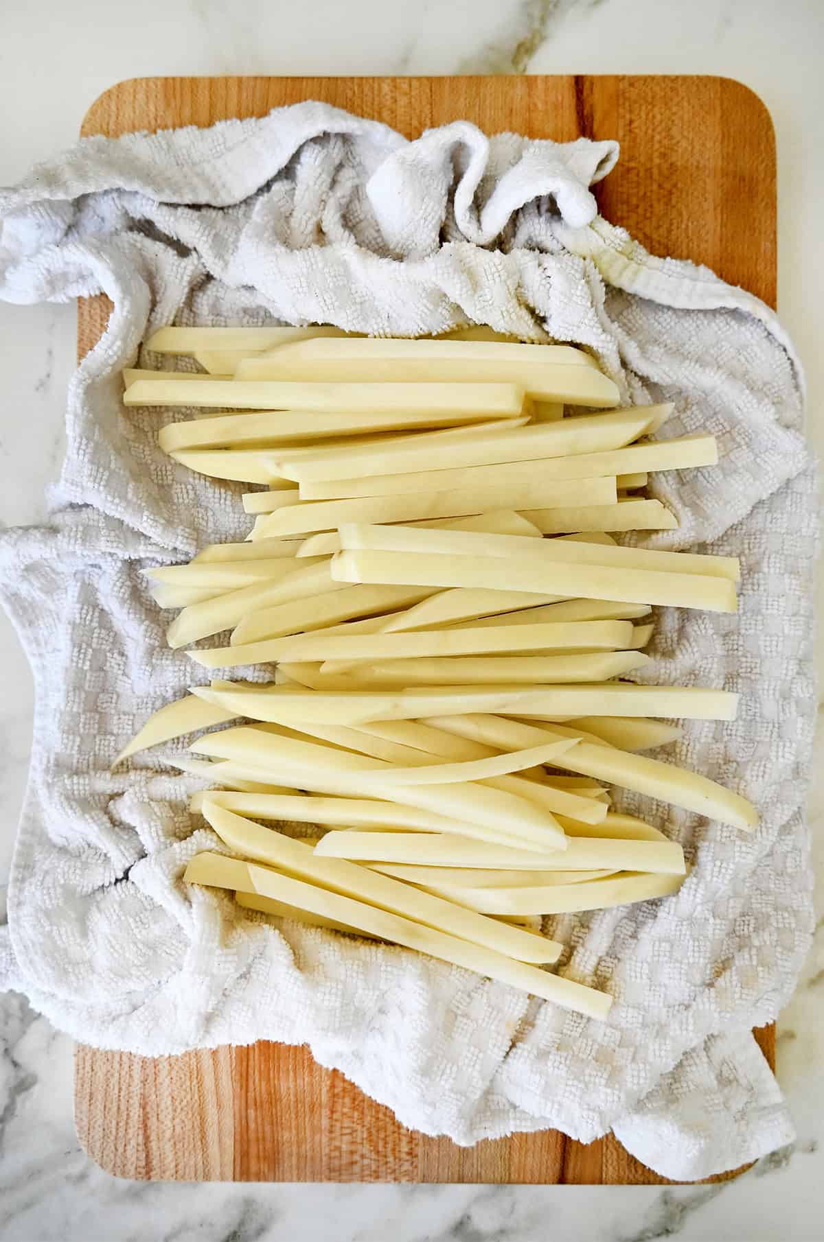 Potato batons drying on a kitchen towel after soaking in water.