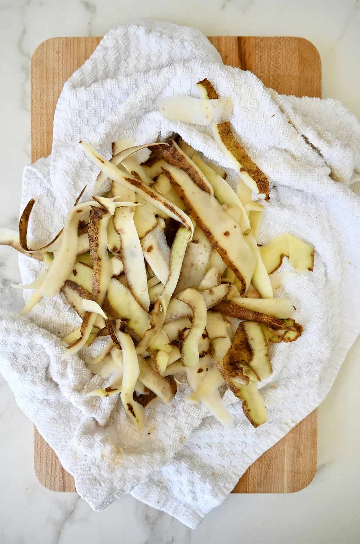 Potato skins drying on a paper towel after soaking in an ice water bath with vinegar.