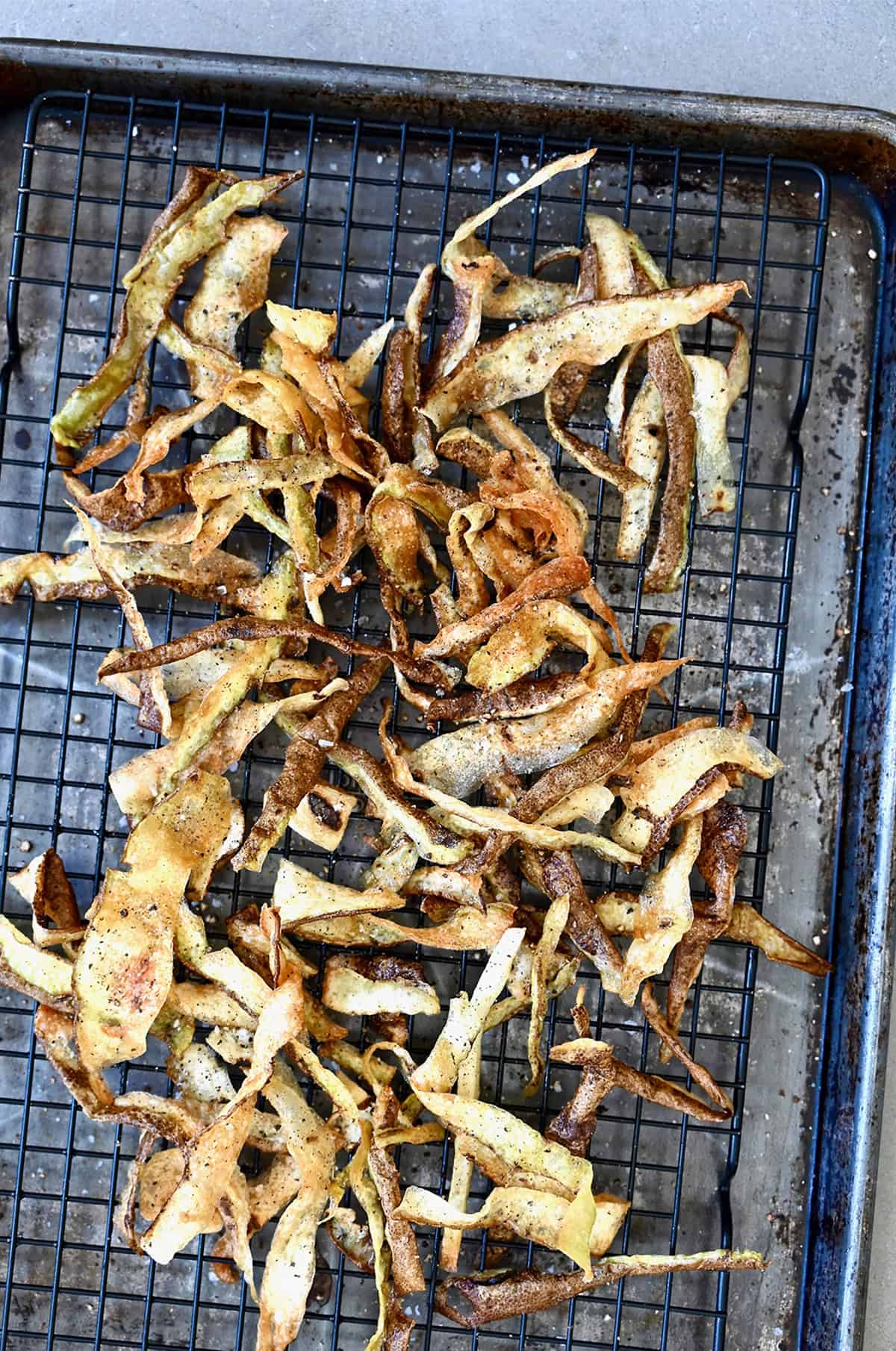 Deep-fried potato chips on a wire rack on top of a baking sheet.