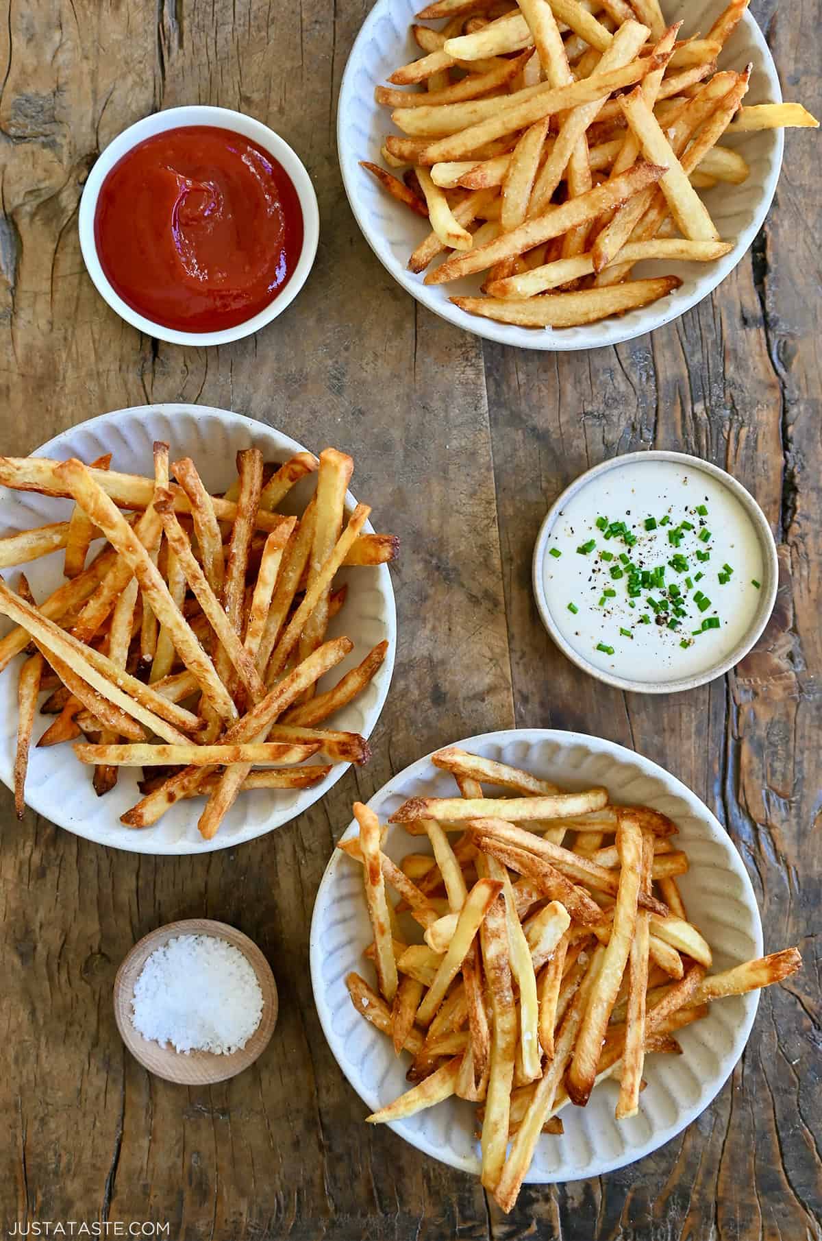 French fries three ways: deep fried, air fried and baked. Three smalls bowls containing ketchup, ranch dressing and sea salt are nearby.