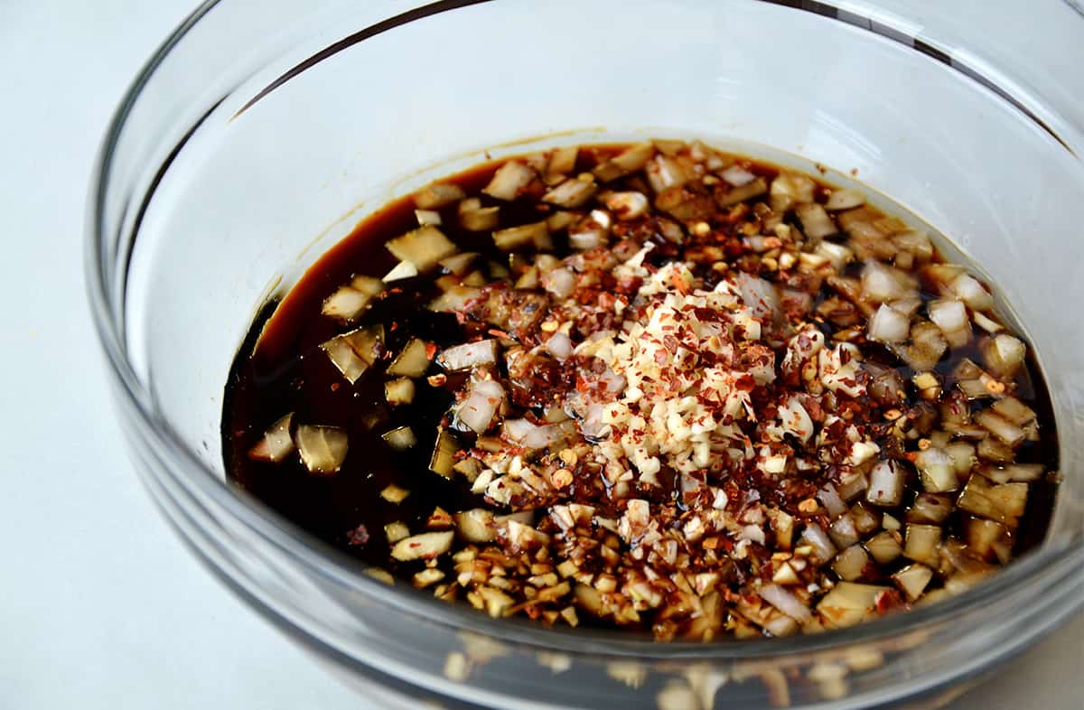 A glass bowl containing honey, soy sauce, blackberry jam, hoisin sauce, minced garlic and diced onion.