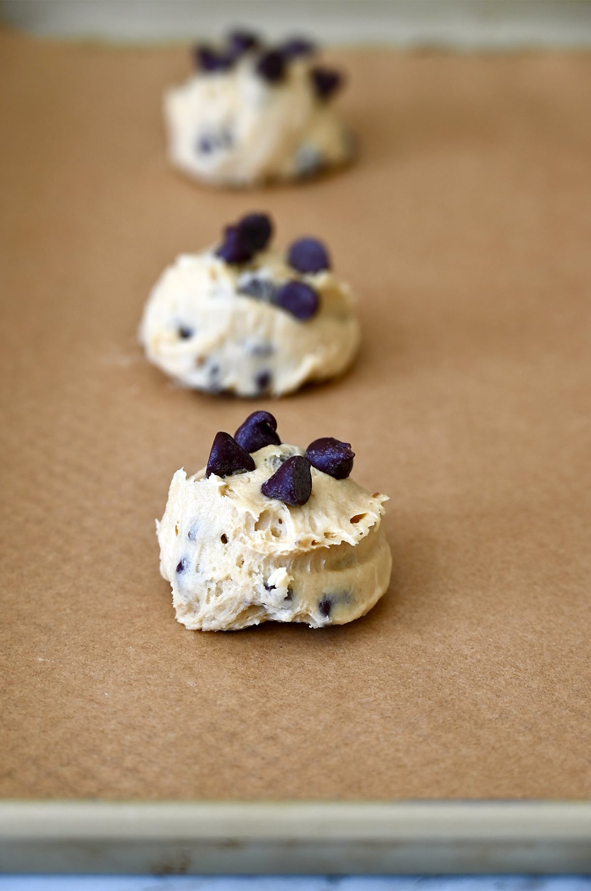 Cookie dough mounds studded with chocolate chips on a baking sheet.