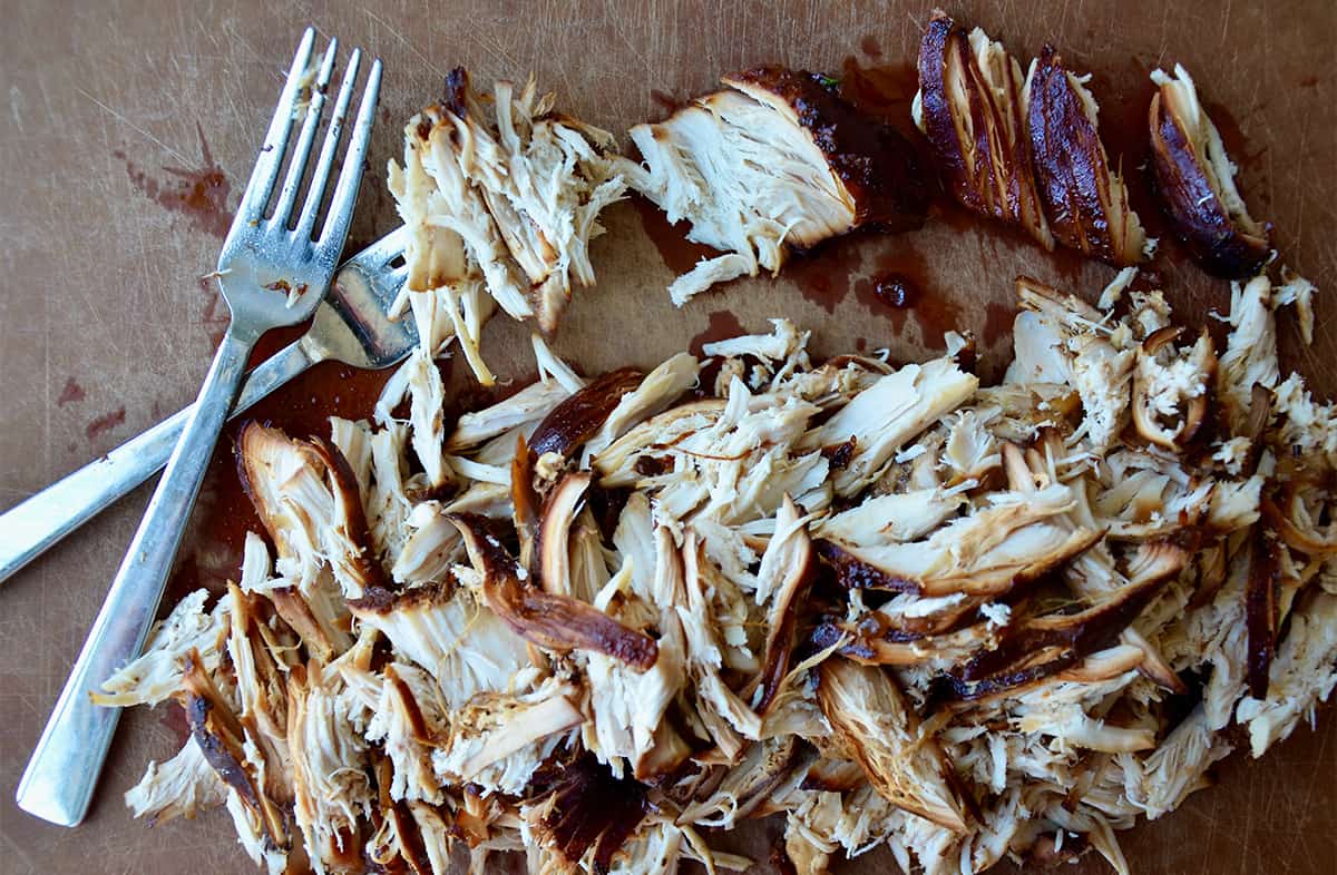 Two forks next to a pile of shredded chicken on a cutting board.