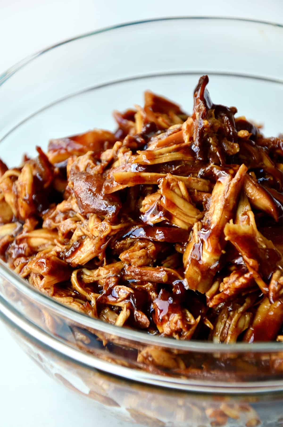 Pulled honey garlic chicken in a glass bowl.