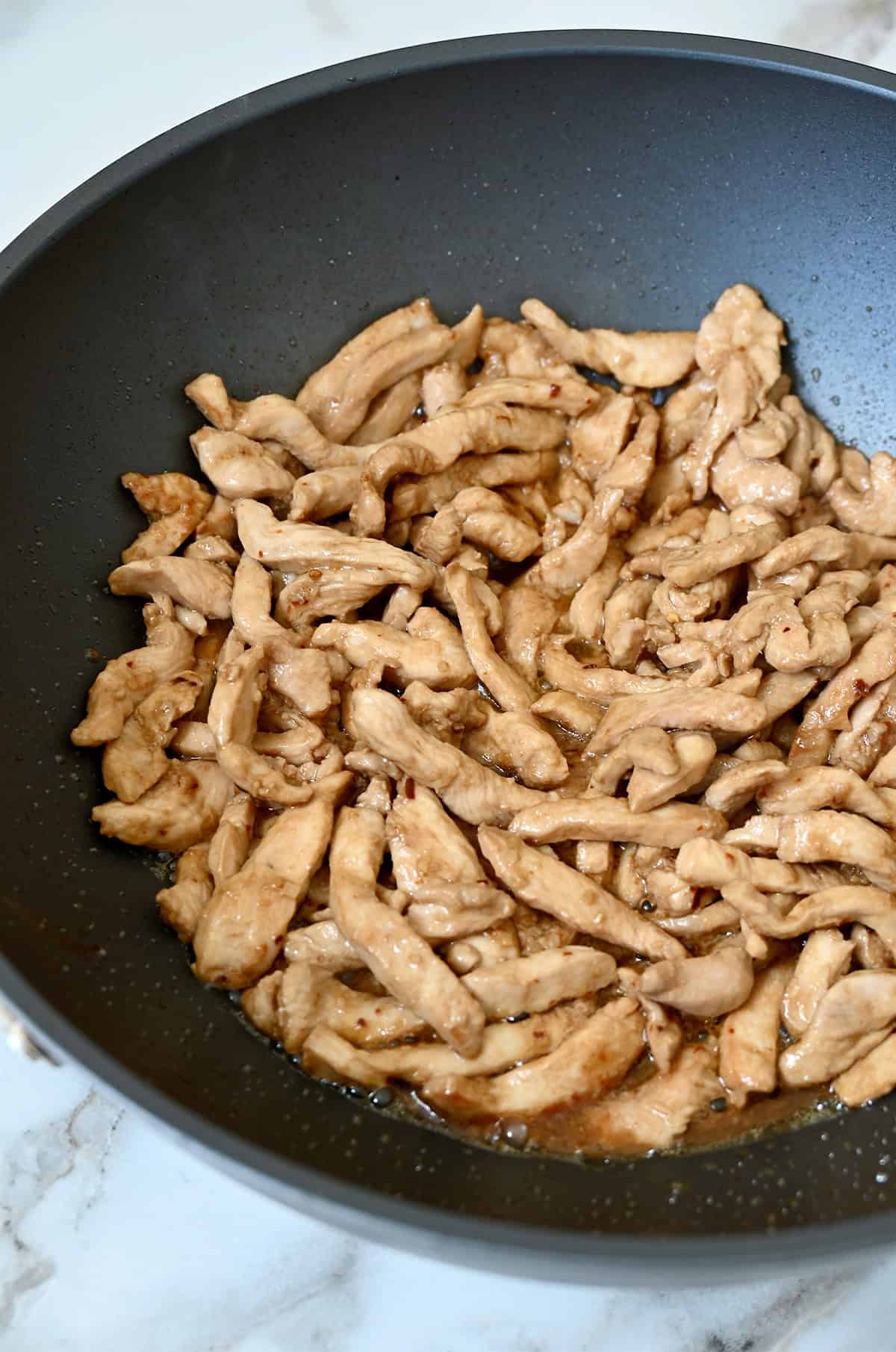 Thin slices of cooked chicken in a wok.