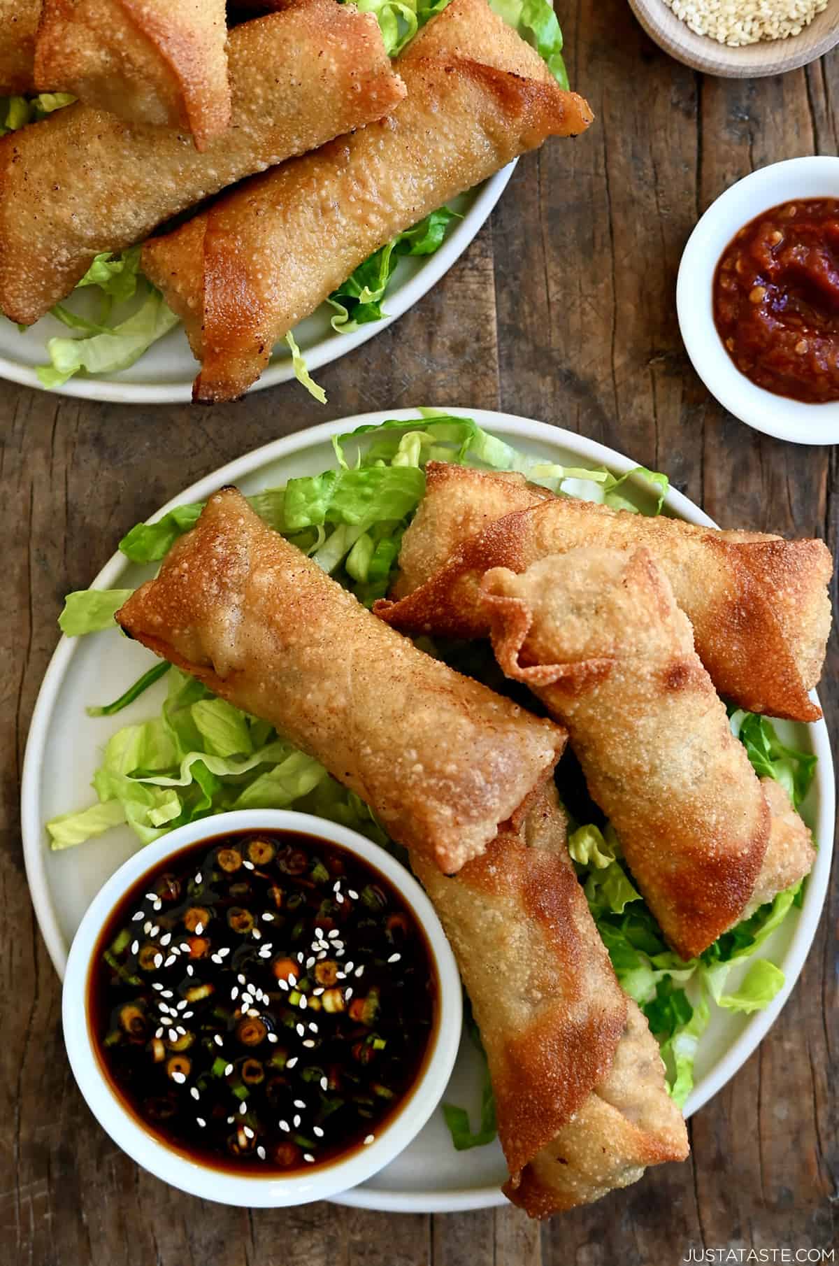 Four crispy pork egg rolls atop shredded lettuce on a plate with a small bowl containing ginger soy dip.