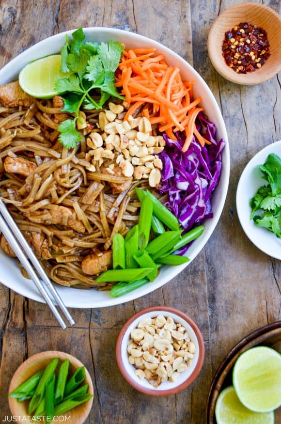 Easy Pad Thai with Chicken on a plate with chopsticks, cilantro, shredded carrots, shredded purple cabbage, scallions and peanuts