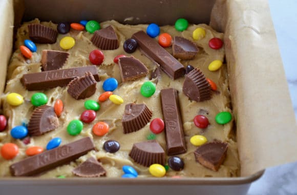 Square baking pan lined with parchment paper containing blondie batter studded with candy