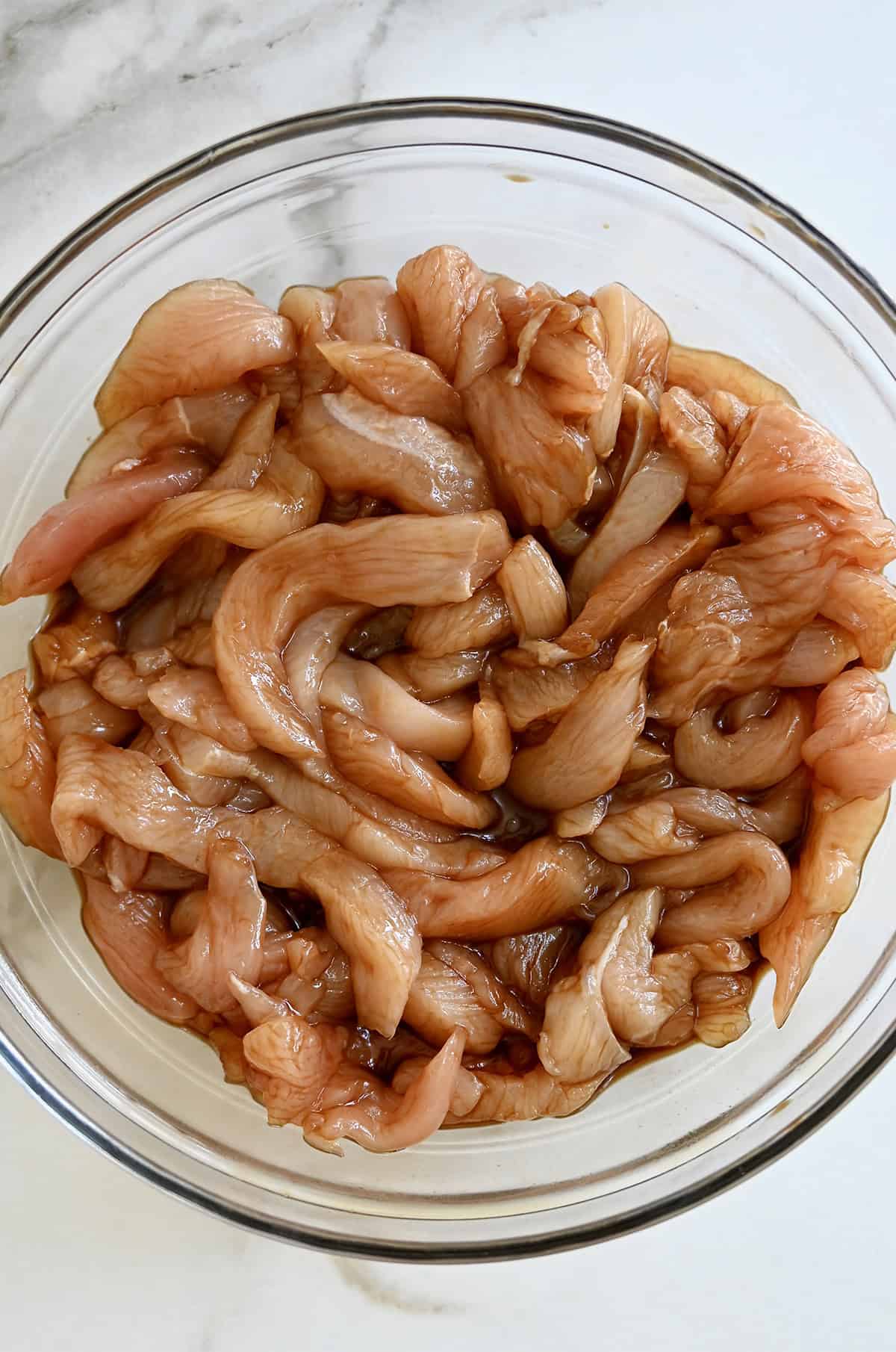 Chicken marinating in a soy sauce and cornstarch mixture in a glass bowl.