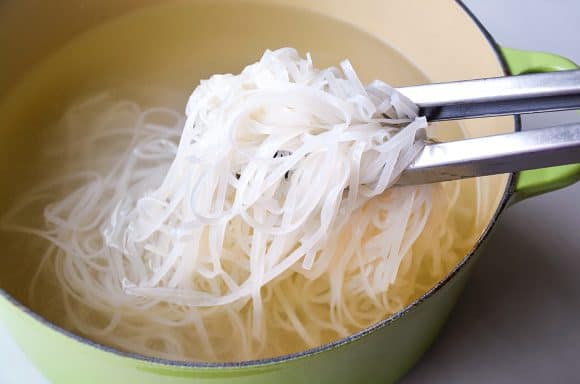 Tongs holding rice noodles over large stockpot