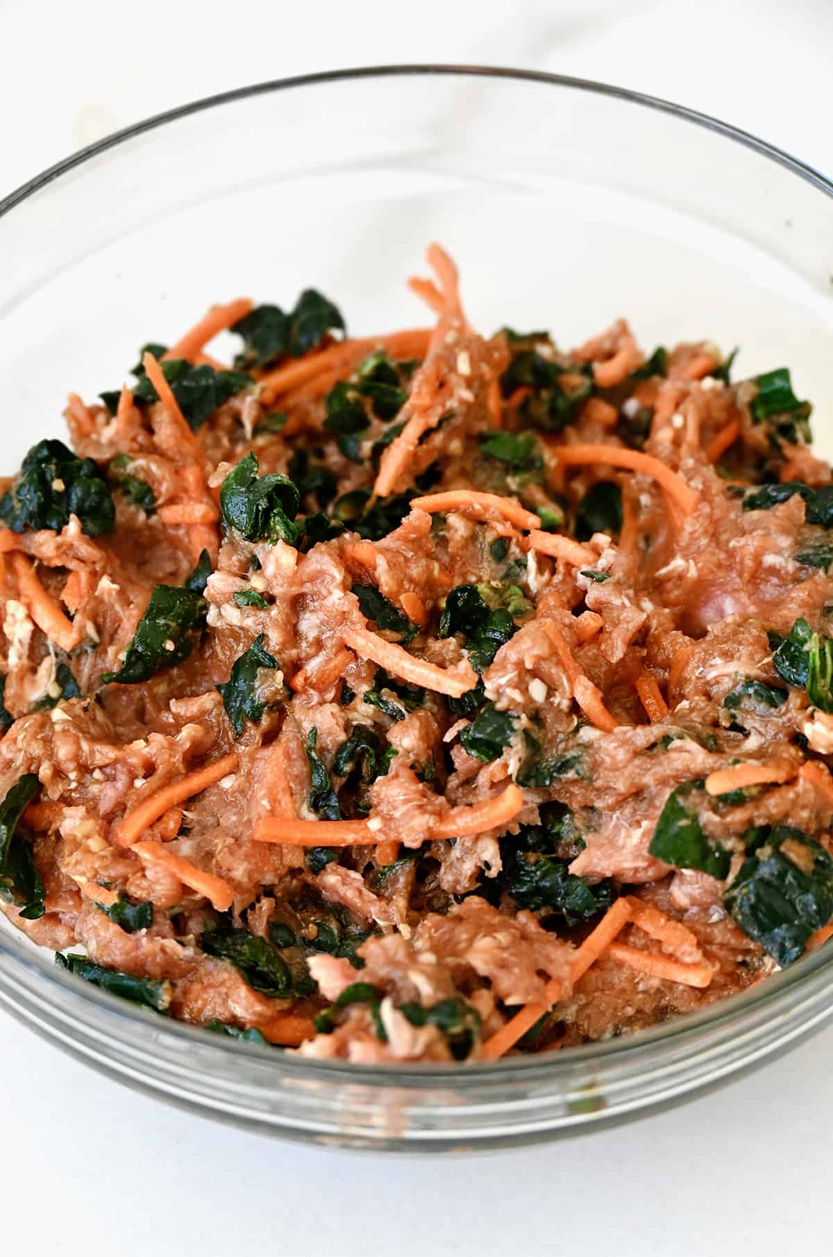 Ground pork, kale and shredded carrots in a glass bowl.