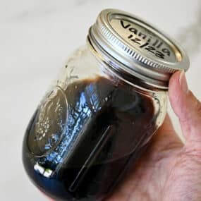 A hand holds a mason jar filled with homemade vanilla extract.