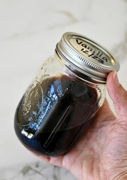 A hand holds a mason jar filled with homemade vanilla extract.