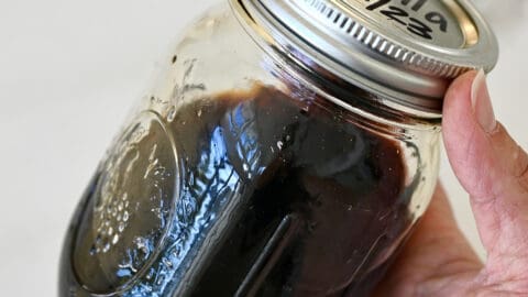 A hand holds a mason jar filled with homemade vanilla extract.