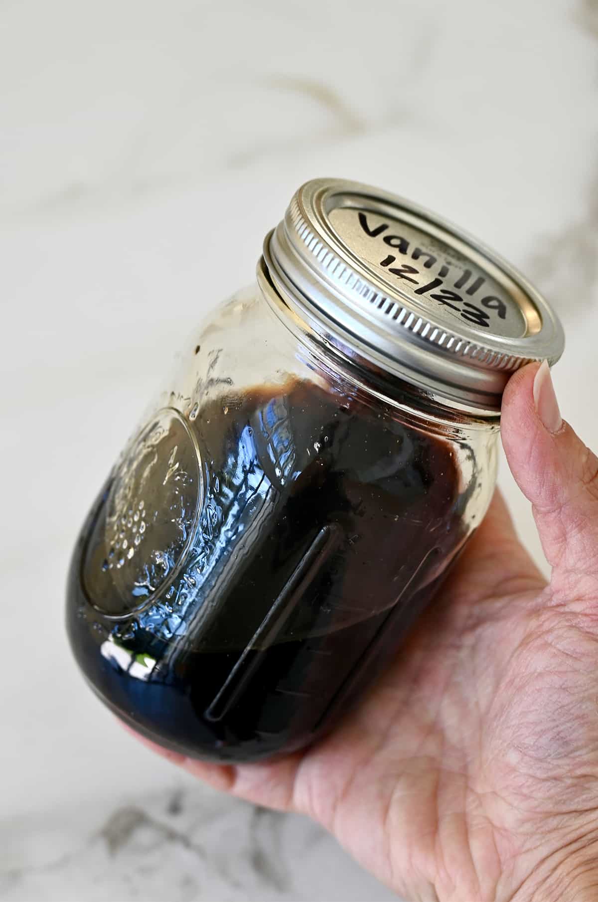 A hand holds a mason jar filled with homemade vanilla extract.
