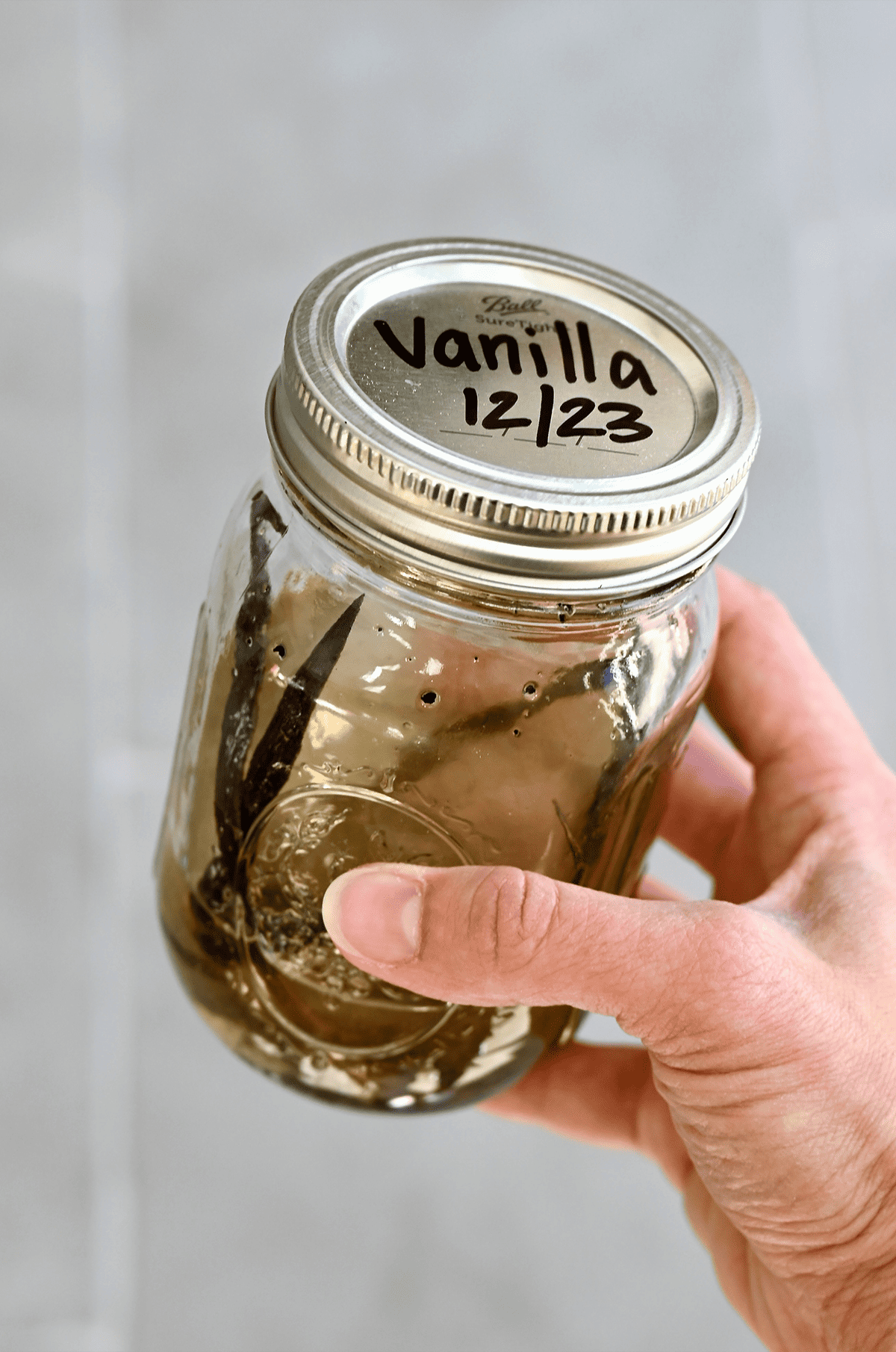 Vanilla bean pods and vodka in a mason jar labeled "Vanilla 12/23."