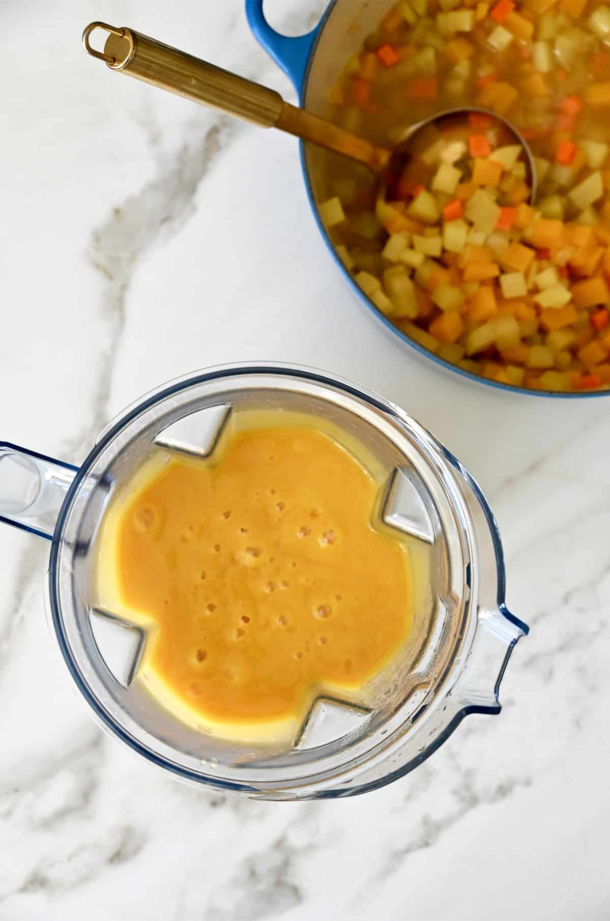 A blender containing creamy squash soup next to a large stockpot containing chopped veggies in chicken stock.