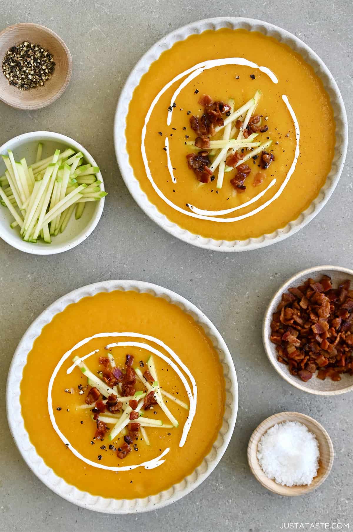 Two bowls containing butternut squash apple soup garnished with crispy bacon, slices of Granny Smith apples and a drizzle of sour cream. 