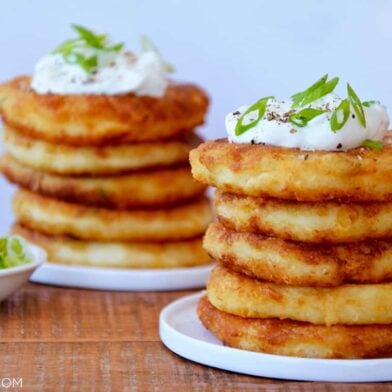 Stacks of mashed potato pancakes on white plates and a small bowl of scallions