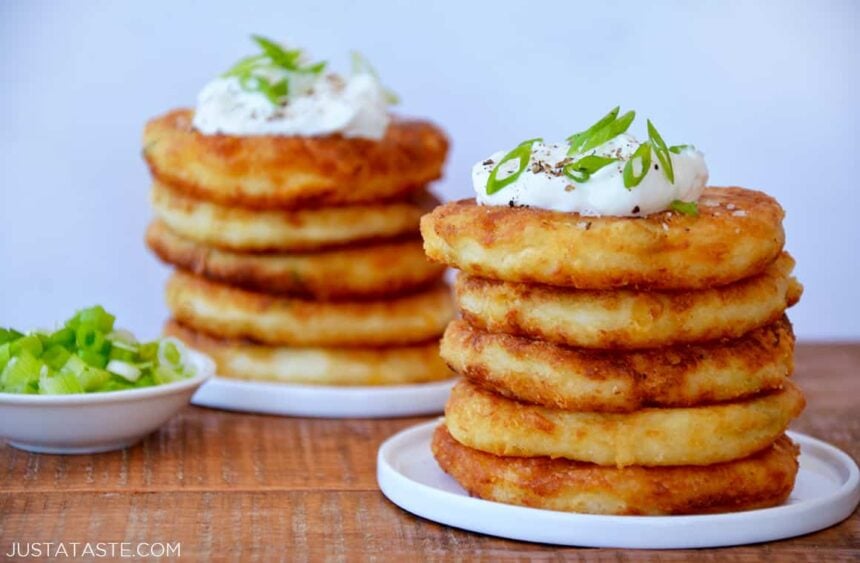 Stacks of mashed potato pancakes on white plates and a small bowl of scallions