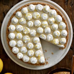 A top-down view of a cheesecake topped with dollops of whipped cream and lemon zest.